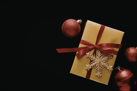 A gold gift box with a red ribbon and a gold snowflake decoration, surrounded by red Christmas...