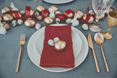 a white plate with a red napkin and gold and silver ornaments on a table with gold utensils and a...