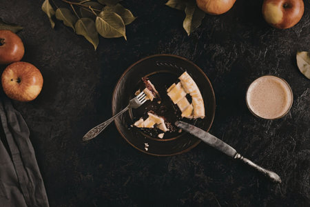 A plate with a slice of apple pie, a fork, and a knife, surrounded by apples and a cup of coffee on...