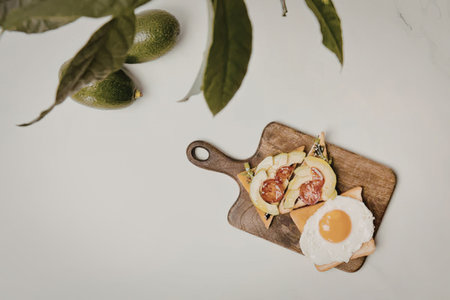 A wooden board with a fried egg, avocado, and tomatoes on toast