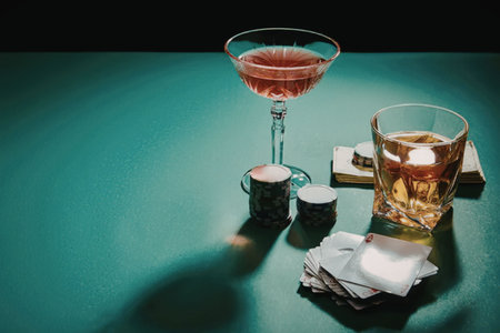 A martini glass and a whiskey glass with a stack of napkins on a green table.