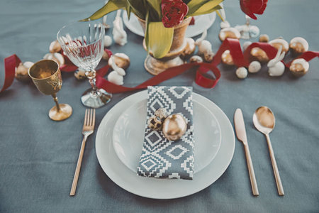 A beautifully set table with a white plate, gold utensils, and a decorative napkin, surrounded by Christmas decorations.の写真素材