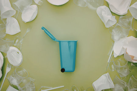 A blue reusable straw cup surrounded by white flower petals and utensils on a green background