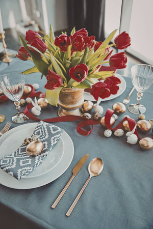 A beautifully set table with red tulips in a vase, gold utensils, and decorative plates.