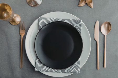 A beautifully set table with a black plate, white plate, copper cutlery, and decorative napkin