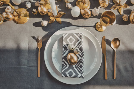 A beautifully set table with gold accents, white plates, and a decorative napkin.の写真素材