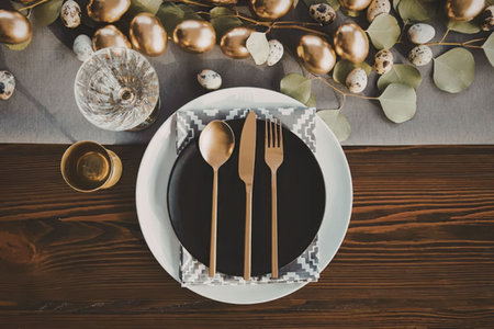 A beautifully set table with golden utensils on a white plate, surrounded by festive decorations.