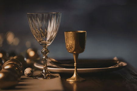 A close-up of two wine glasses, one crystal clear and the other metallic gold, placed on a dark...