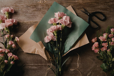a bouquet of pink flowers on a wooden table with scissors and wrapping paperの写真素材