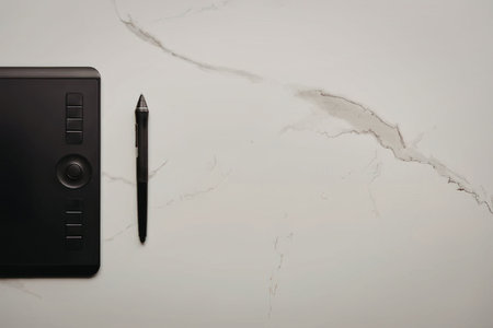 A black graphic design tablet and stylus on a white marble surface