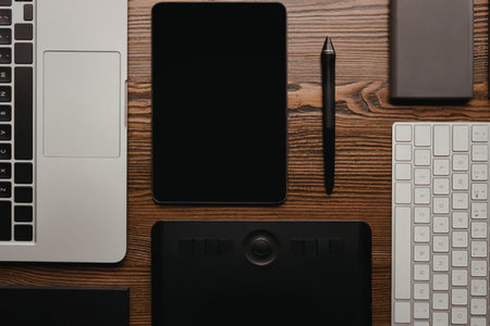A workspace with a laptop, graphics tablet, stylus, smartphone, and keyboard on a wooden desk.