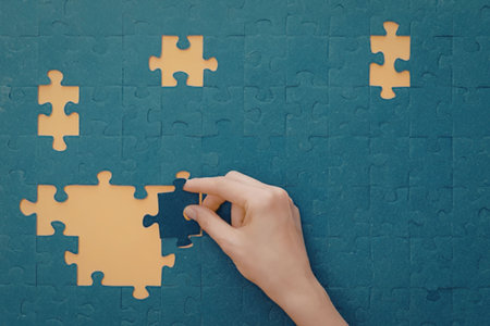 A hand placing a puzzle piece into a partially completed jigsaw puzzle on a blue background.