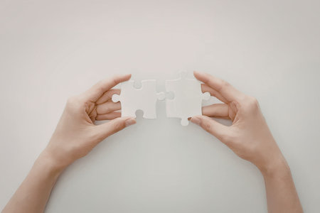 A pair of hands holding two puzzle pieces against a white backgroundの写真素材