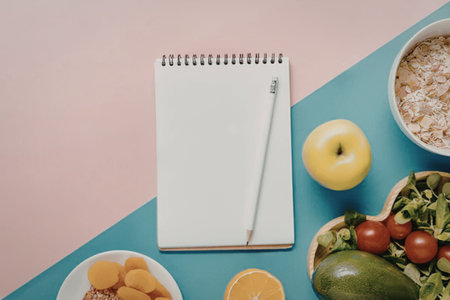 A flat lay of healthy food items and a notebook on a pink and blue background.の写真素材