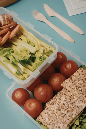A plastic container filled with healthy food including tomatoes, lettuce, carrots, and crackers.の写真素材