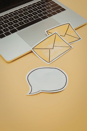 A laptop with email icons and a speech bubble on a yellow background