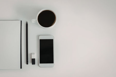 A neatly arranged office desk with a notebook, pen, phone, eraser, and a cup of coffee on a clean...
