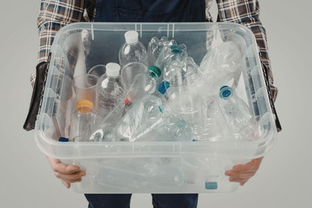 A person holding a clear plastic bin filled with various used plastic bottles.
