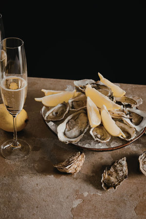 A plate of oysters with lemon wedges and two glasses of champagne on a tableの写真素材