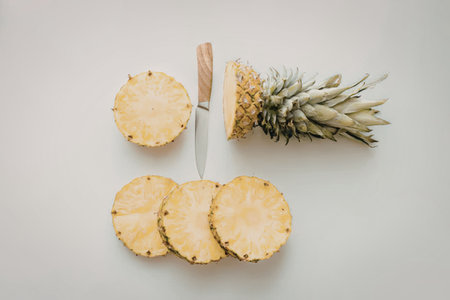 Pineapple slices and a knife on a white surface