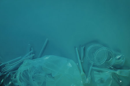 An underwater scene depicting various plastic items such as bottles, straws, and other disposable...