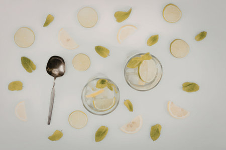Two glasses of cucumber and lemon infused water with slices of cucumber and lemon, and leaves, on a white background with a spoon.の写真素材
