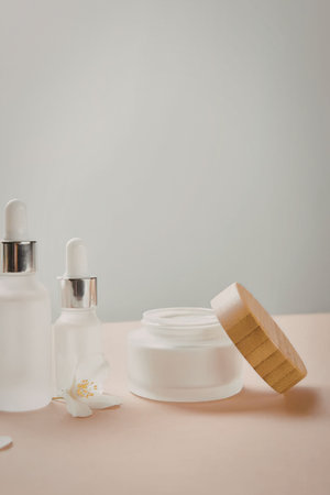 The image shows a selection of skincare products arranged on a table, including two dropper bottles and a jar of cream with its lid leaning against it.の写真素材