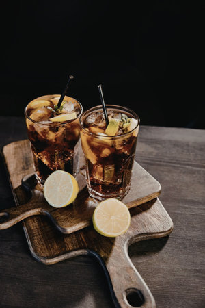 Two glasses of iced tea with lime slices and straws on a wooden board