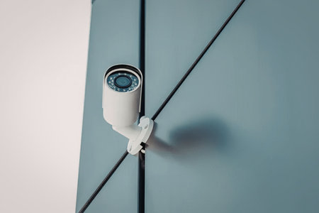 A white security camera mounted on a blue wall with black lines