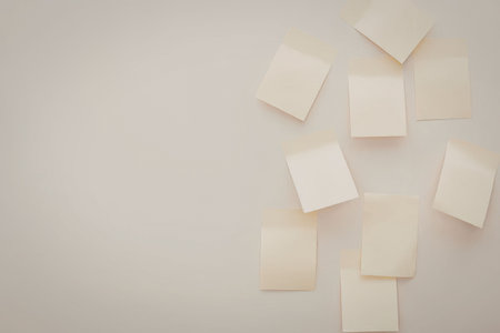 A collection of yellow sticky notes scattered on a beige surface, with some notes overlapping or partially out of frame.の写真素材