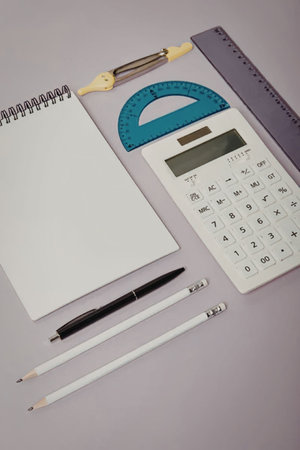 A collection of school supplies including a notebook, calculator, ruler, pencils, and protractor arranged on a purple background.の写真素材