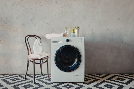 A washing machine and a chair are placed in a room with a concrete wall and patterned floor.の写真素材