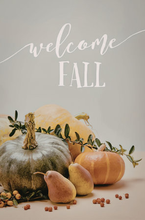 A collection of pumpkins and fruits arranged with greenery and berries on a table with a welcome to fall messageの写真素材