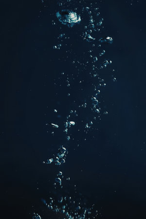 An image of a stream of bubbles rising through dark blue water, showcasing the beauty of underwater scenes.の写真素材