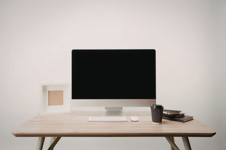 A modern workspace setup featuring a computer monitor, keyboard, mouse, and a cup on a wooden desk...