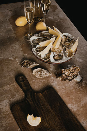 A plate of oysters with lemon wedges on a table with glasses of champagneの写真素材
