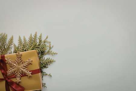 A gold-wrapped gift adorned with a red ribbon and a gold snowflake, accompanied by green pine...