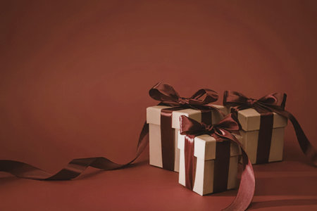 Two elegantly wrapped gifts with red ribbons on a matching red background, perfect for festive occasions.の写真素材
