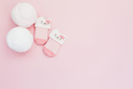 A pair of pink and white baby socks with a cute animal design are placed next to two white balls on a soft pink background. The socks have a sweet and playful look, making them perfect for a baby's nursery or a gift for a new parent.