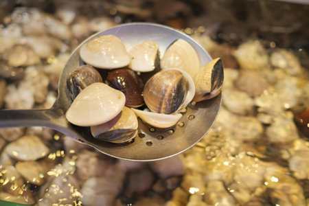 Close-up of fresh clams in a bowl against a sandy beach setting.