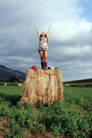 young girl standing on the haystack raises his hands to the skyの写真素材