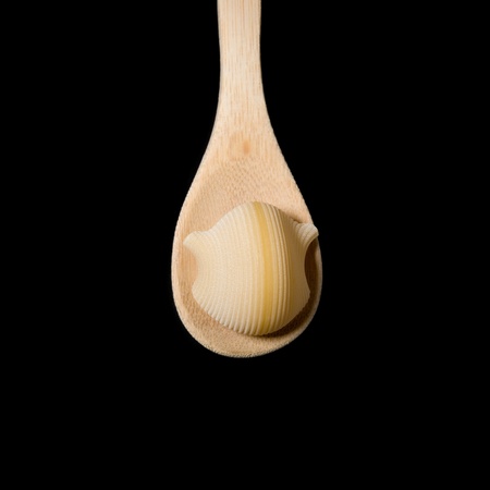 Raw pasta on a wooden spoon on a black backgroundの写真素材