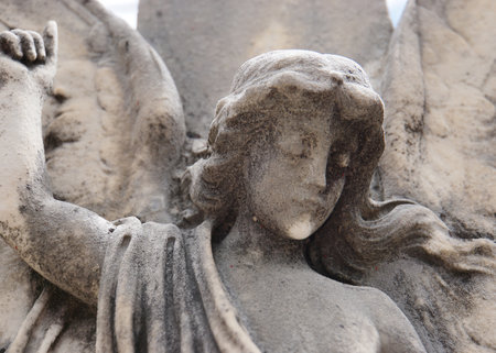 Close up with detail of a robed female carved stone angel with open wings, raised arm and long hair includes highlights and shadows over the stone with texture detail.のeditorial素材