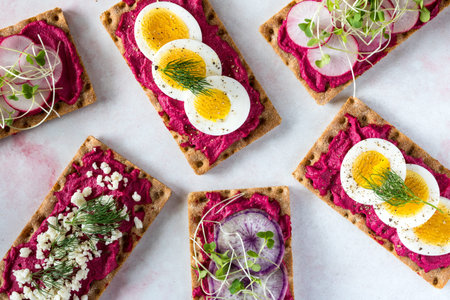 Top down view of rye wafer crackers and beet hummus with a variety of healthy toppings and garnish ready for eating.の写真素材