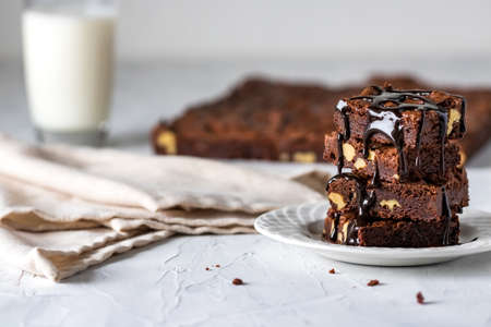 Front view of a small stack of chocolate brownies covered in chocolate sauce against a blurred backgroundの写真素材