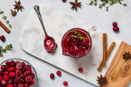 Top down view of homemade whole berry cranberry sauce surrounded by cranberries, cinnamon sticks and...