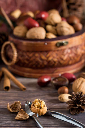 A close up of a woven basket of mixed nuts with a nut cracker cracking open a walnut in front.の写真素材