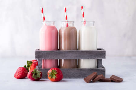 A close up view of three glass jars of strawberry, chocolate and vanilla flavoured milkshakes ready for drinking. の写真素材