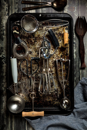 A top down view of an abstract arrangement of antique utensils on a baking sheet against a dark...