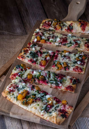 Top down view of slices of vegetable flatbread pizza on a wooden cutting board.の写真素材